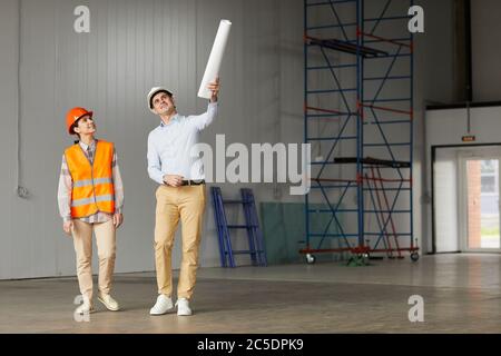 Ingenieur in Arbeit Helm zeigt auf etwas und erklärt den Prozess der Arbeit an Arbeitnehmer sie in leerem Gebäude stehen Stockfoto