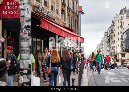 Paris, Frankreich - 18. Juni 2015: Ein lockiger Mann in einem grünen Pullover geht die Straße entlang und telefoniert. Menschen, die den Bürgersteig entlang gehen Stockfoto