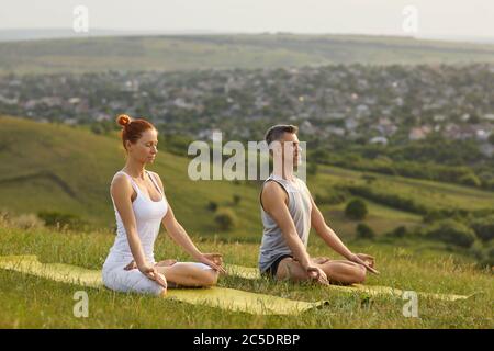 Yoga in der Natur. Millennial Paar macht Yoga-Meditation in den Bergen. Mann und Frau üben im Freien Atemübungen Stockfoto