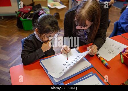 Eine Lehrerin hilft einem Schulmädchen während eines Englischunterrichts in Großbritannien Stockfoto