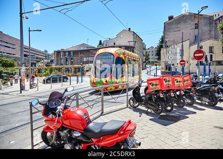 MONTPELLIER, FRANKREICH - 24. Juni 2015: Öffentliche Verkehrsmittel in der Stadt. Schöne mehrfarbige Straßenbahn. Rote Motorrad und Roller für die Lieferung von Fast Food in der Stockfoto