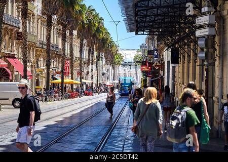 MONTPELLIER, FRANKREICH - 24. Juni 2015: Menschen, die die Straße durch Straßenbahnlinien überqueren. Blick auf eine Stadtstraße mit Anwohnern, Touristen, grünen Palmen und Stockfoto