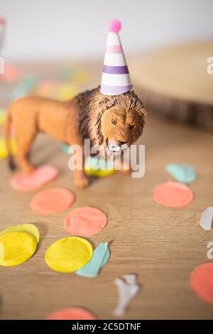 Kunststoff-Löwen-Spielzeug mit Party Hut auf einem bunten Spots Holztisch Stockfoto