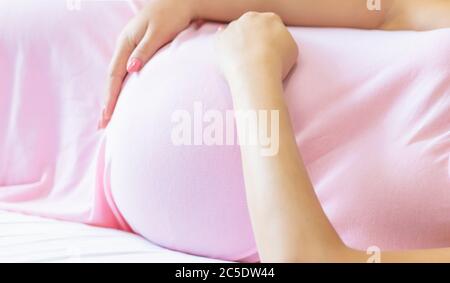 Eine schwangere Frau im Bett umarmt ihren Bauch. Selektiver Fokus. Menschen. Stockfoto