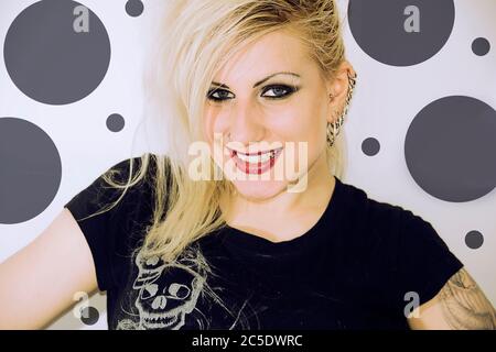 Ziemlich junge blonde Mädchen mit Piercings lächeln auf einem gepunkteten Hintergrund. Stockfoto