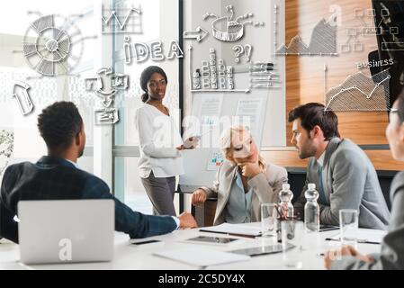 Attraktive afroamerikanische Geschäftsfrau, die neben dem Flipchart mit Infografiken steht, während multikulturelle Kollegen am Schreibtisch sitzen, Business-Illustrat Stockfoto