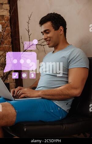 Lächelnd gemischtes Rennen Freiberufler mit Laptop in der Nähe von virtuellen Sprechblase mit Chat Stockfoto