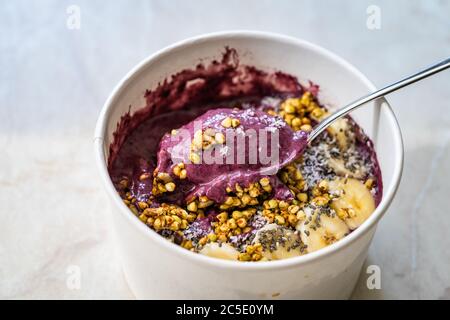 Take Away Vegane Lebensmittel Acai Schale mit Mandelmilch, Erdnussbutter, Banane, Buchweizen Müsli, Chia Samen und Schokoladenstücke in Karton Schüssel. Gesunde Org Stockfoto