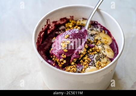 Take Away Vegane Lebensmittel Acai Schale mit Mandelmilch, Erdnussbutter, Banane, Buchweizen Müsli, Chia Samen und Schokoladenstücke in Karton Schüssel. Gesunde Org Stockfoto