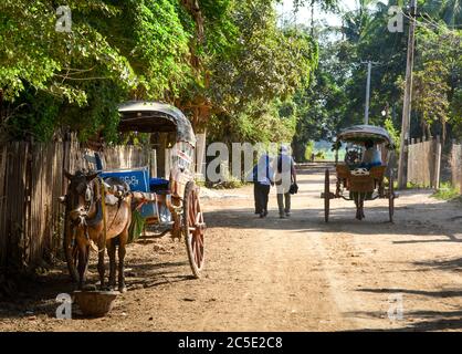 Kutsche und ein paar alte Reisende auf Landstraße in Inwa, oder Ava, Mandalay, Myanmar, Südostasien. Rucksackreisen in friedlicher Landschaft. Stockfoto