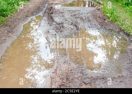 Schmutzige Straße mit Pfütze während der Regenzeit, Pfütze in Feldweg Stockfoto