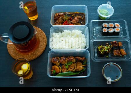 Asiatische Küche, Sushi, Brötchen, Reis und Hähnchenspieße. Essen in Einweggeschirr. Bestellen Sie asiatische Speisen zu Hause. Stockfoto