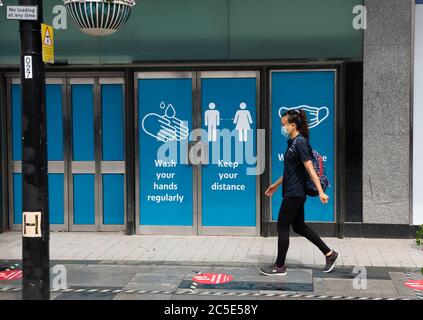 Slough, Berkshire, Großbritannien. Juli 2020. Ein Mädchen trägt eine Gesichtsmaske, während sie an Schildern für Käufer in Slough High Street vorbeigeht und sie daran erinnert, wie man versucht, Coronavirus zu verhindern. Quelle: Maureen McLean/Alamy Stockfoto