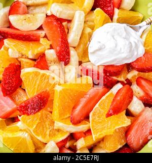 Obstsalat mit Erdbeeren, Orangen, Bananen und saurer Sahne Hintergrund Stockfoto