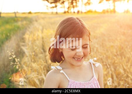 Lustiges Mädchen lacht bei einem Spaziergang über das Feld bei Sonnenuntergang. Das Konzept der echten Kindheit, digitale Entgiftung, Sommerferien, Glück.