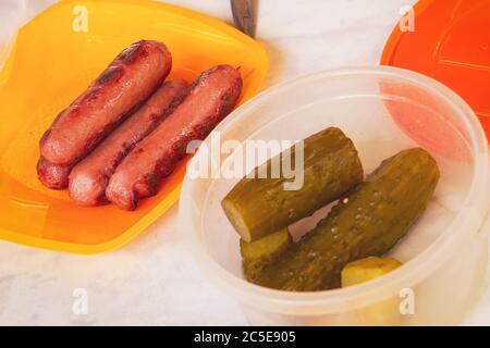 Gegrillte Würstchen und Gurken in Plastikgeschirr. Einweggeschirr Stockfoto
