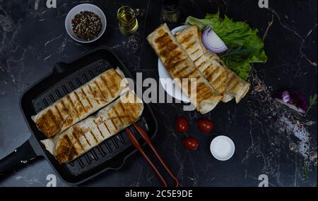 Gegrilltes Hähnchen Shawarma mit Gewürzen und Gemüse. Shawarma auf einer Grillpfanne. Shawarma auf einem dunklen Hintergrund. Stockfoto
