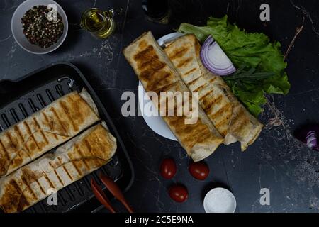 Gegrilltes Hähnchen Shawarma mit Gewürzen und Gemüse. Shawarma auf einer Grillpfanne. Shawarma auf einem dunklen Hintergrund. Stockfoto