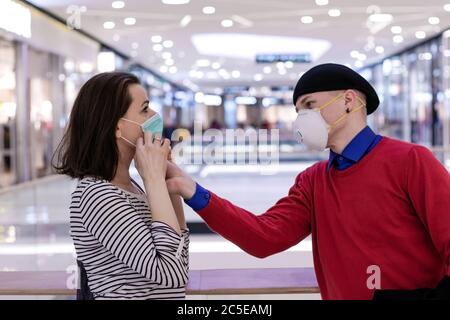 Junges Paar im Einkaufszentrum reden, tragen zwei verschiedene Arten von Schutzmasken zum Schutz vor Viren. Ausbruch des Coronavirus. Stockfoto