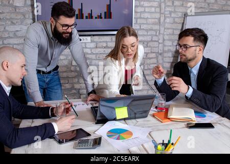 Team von jungen Geschäftsleuten und Designern, vor einem Laptop-Computer versammelt, an neuen Projekten arbeiten und diskutieren neue Geschäftsideen. Stockfoto
