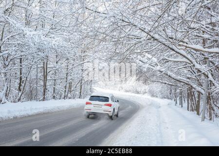 Straße im Winterwald. Weißes Auto geht durch Wälder nach Schneefall. Landschaftlich schöner Blick auf den Tunnel mit verschneiten Bäumen. Schöne Landschaft von gefrorenem Weg bedeckt Schnee. Stockfoto