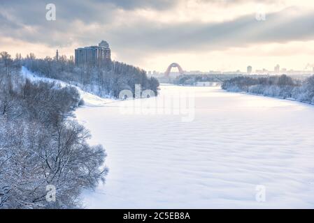 Winterlandschaft in Moskau, Russland. Landschaft des Moskwa Flusses bedeckt Eis und Schnee in Sonnenlicht. Landschaftlich schöner Blick auf den gefrorenen Fluss im Hintergrund. Verschneite Natur Stockfoto