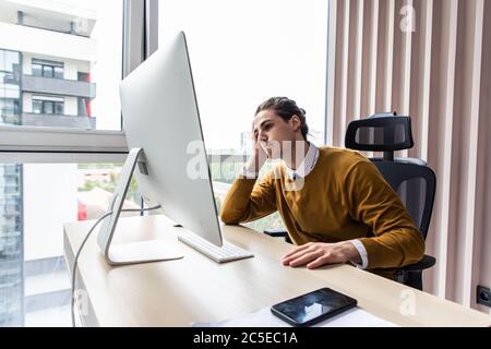 Frustrierter Geschäftsmann, der im Büro mit der Hand am Kopf sitzt Stockfoto