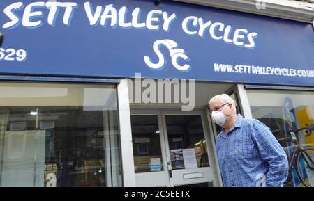 Ein Mann mit Gesichtsmaske geht an Sett Valley Cycles auf der Union Road, New Mills, Derbyshire vorbei. Stockfoto