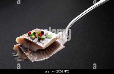 Stücke von gesalzenem Hering auf Gabel auf schwarzem Hintergrund Stockfoto