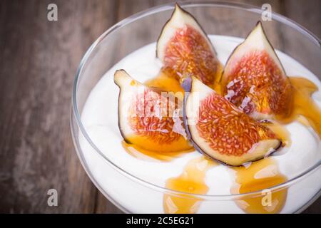 Griechischer Joghurt mit Feigen und Honig, in einer Glasschale auf altem Holzhintergrund Stockfoto