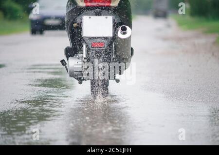 Motorrad Moped fährt durch eine Pfütze auf einer nassen Straße im Regen. Spray fliegt von den Rädern. Nahaufnahme Stockfoto