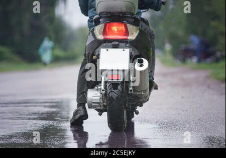 Motorrad Moped fährt durch eine Pfütze auf einer nassen Straße im Regen. Spray fliegt von den Rädern. Nahaufnahme Stockfoto