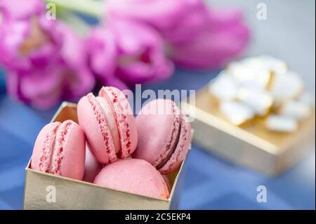 Traditionelle französische Mandeln liegen in Reihen in einer Geschenkbox auf dem Hintergrund eines Blumenstraußes. Nahaufnahme, selektiver Fokus. Stockfoto