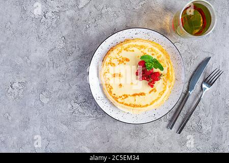 Pfannkuchen mit karamellisierten Äpfeln, Himbeeren, Erdbeeren und roten Johannisbeeren. Brunch mit grünem Tee und Crepes. Stockfoto