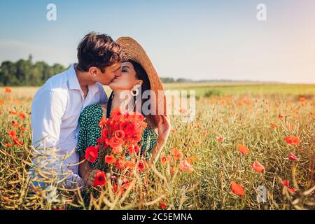 Liebevolles Paar küssen in Mohn Feld mit Blumenstrauß. Glücklicher junger Mann umarmt Frau. Sommerurlaub Stockfoto