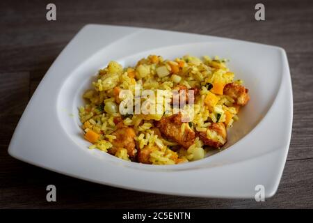 Paella mit Fleisch, Pfeffer, Gemüse und Gewürzen auf dem Teller Stockfoto