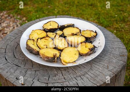 Gebackene Kartoffeln im Gartenfeuer auf einem Teller serviert Stockfoto