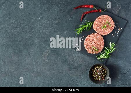 Rohe Burger-Cutlets aus Hackfleisch mit Rosenfleisch und Chili auf einem Schieferbrett Draufsicht. Zutaten für die Herstellung von Burgern. Speicherplatz kopieren. Stockfoto