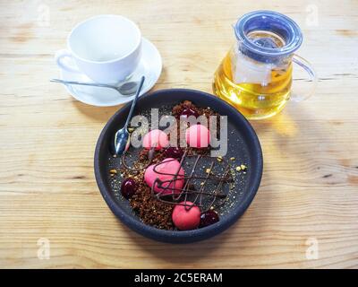 Ein Teller mit einem rosa Dessert, eine transparente Teekanne und eine saubere Tasse auf einer Untertasse auf einer Holztheke Stockfoto