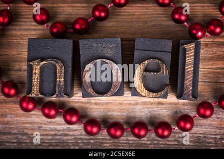 Das Wort NOEL mit Vintage-Holz-Druckerblöcke geschrieben. Weihnachtsbotschaft über altem Holz mit einer Schnur dekorativer roter Perlen. Stockfoto