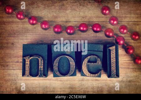 Das Wort NOEL mit Vintage-Holz-Druckerblöcke geschrieben. Weihnachtsbotschaft über altem Holz mit einer Schnur dekorativer roter Perlen. Stockfoto
