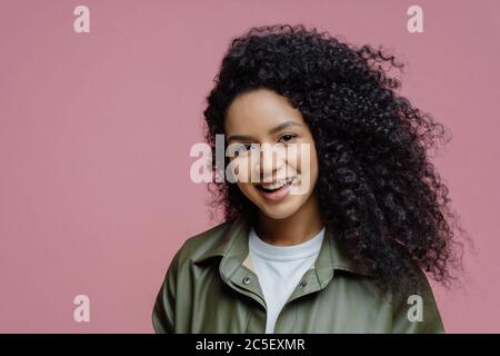 Nahaufnahme Porträt von lächelnd junge weibliche Modell hat lockiges Haar, gesunde Haut, schaut direkt auf die Kamera, drückt positive Emotionen, genießt phot Stockfoto