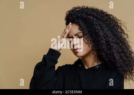 Seitliches Schuss von unzufrieden dunkelhäutigen Frau berührt Stirn, leidet Kopfschmerzen und Mirgain, squints Gesicht von Schmerzen, braucht Schmerzmittel, kann nicht konz Stockfoto