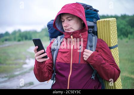Wanderer Reisende mit einem großen Rucksack schaut auf eine Karte in seinem Smartphone. Stockfoto