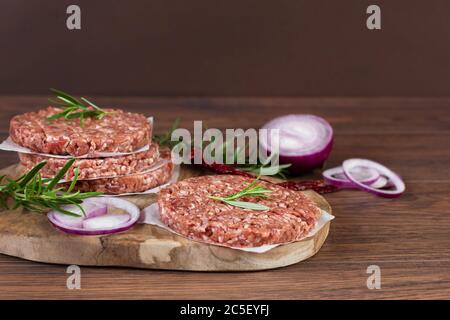 Rohe Burger-Cutlets aus Hackfleisch frisch treffen auf Gewürzen und Kräutern auf Holzhintergrund. Zutaten für die Herstellung von Burgern. Stockfoto