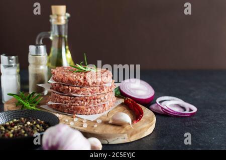 Rohe Burger-Cutlets aus Hackfleisch frisch treffen auf Gewürze und Kräuter auf schwarzem Hintergrund. Zutaten für die Herstellung von Burgern. Stockfoto