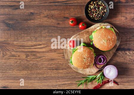 Rindfleisch-Burger mit frischem Salat, Käse, Tomaten und Pfeffer Gewürz auf Holz Hintergrund Draufsicht. Fast Food. Stockfoto