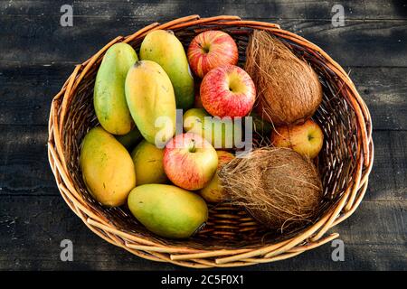 Früchte, Mango, Kokosnuss, Apfel in einem Korb auf schwarzem Holzgrund mischen Stockfoto