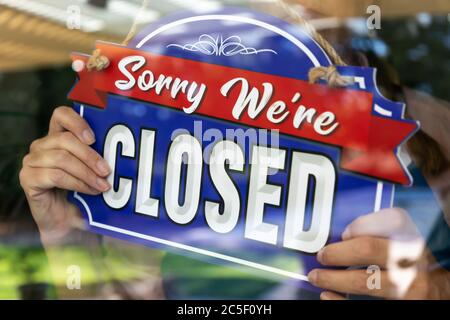 Weibliche Ladenbesitzerin, die das Schild zu „Geschlossen im Fenster“ umdreht. Stockfoto