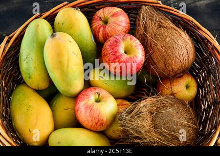 Früchte, Mango, Kokosnuss, Apfel in einem Korb auf schwarzem Holzgrund mischen Stockfoto